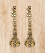 Set of two golden brass sitar-shaped door handles on light wood surface