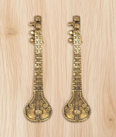 Set of two golden brass sitar-shaped door handles on light wood surface