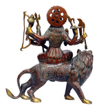 Durga brass statue from behind: seated on lion with many arms and circular back halo