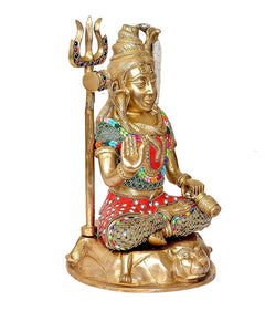 Lord Shiva brass statue seated, facing right, trident in left hand, ornate belt.