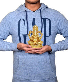 Brass Ganesha idol statue held in hands by a person, seated on a round base.