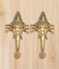 Brass Ganesha face door handle pair on light wood board, symmetrical front view