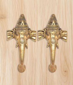 Brass Ganesha face door handle pair on light wood board, symmetrical front view