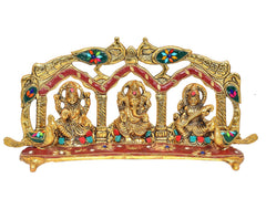 Peacock-framed metal idol featuring three seated deities: Ganesh, Laxmi, Saraswati