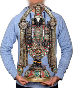 Brass idol statue on pedestal held in hands, showing multicolored jeweled clothing
