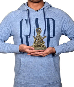 Small 4.5 inch brass Saraswati idol held in hands on a light blue hoodie
