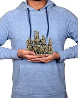 Person holding a small brass Shiv Parivar idol while wearing a light-blue hoodie