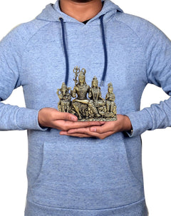 Person holding a small brass Shiv Parivar idol while wearing a light-blue hoodie