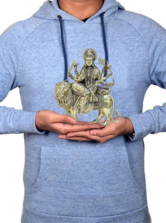 Person holding brass Durga Maa lion idol while wearing a light blue hoodie
