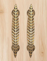 Golden brass leaf-style door handles with round escutcheons on light wood