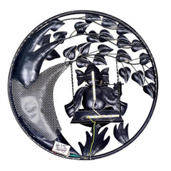 Black-toned round wall hanging of Ganesha on swing playing flute, dark metal leaf vines