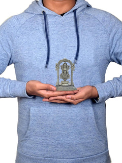 Small brass Lakshmi statue on lotus, held in hands over grey hoodie