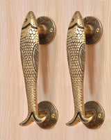Brass fish door handle pair on light wood door, full length handle grips visible.