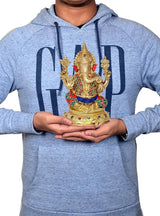 Person holding brass Lord Ganesha idol; statue shows red trunk, jeweled crown and blue sash.