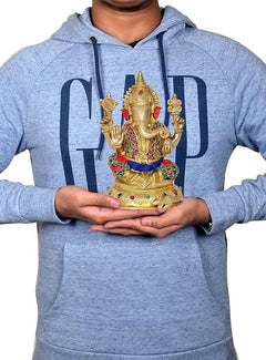 Person holding brass Lord Ganesha idol; statue shows red trunk, jeweled crown and blue sash.