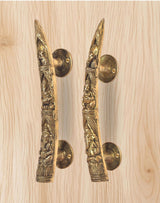 Brass Ganesha door handle pair close-up on light wood, long embossed levers with rosettes
