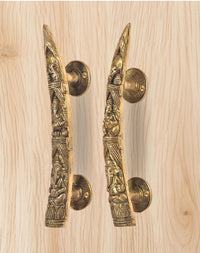 Brass Ganesha door handle pair close-up on light wood, long embossed levers with rosettes