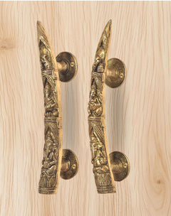 Brass Ganesha door handle pair close-up on light wood, long embossed levers with rosettes