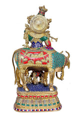 Back view of brass Krishna statue on cow, fan-like halo, colorful panels on base