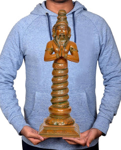Brass Patanjali statue held in hands, showing front face, prayer pose, and pedestal.