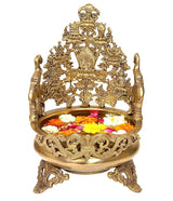Brass urli bowl with ornate figurine stand and decorative flowers inside