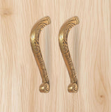 Ornate golden brass pull handles pair with circular end caps and scrollwork.