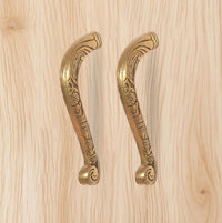 Ornate golden brass pull handles pair with circular end caps and scrollwork.