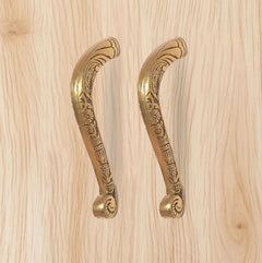 Ornate golden brass pull handles pair with circular end caps and scrollwork.
