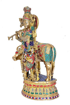 Brass Krishna figurine beside cow, richly painted robe, jewelry, and decorative halo