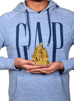 Radha Krishna murti held in hands, small gold-tone deity statue on palms