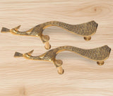 Brass peacock door handle pair laid flat, golden finish on light wood