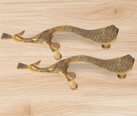 Brass peacock door handle pair laid flat, golden finish on light wood