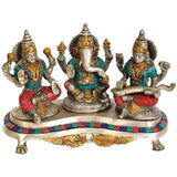 Brass Ganesh-Lakshmi-Saraswati idol trio on pedestal with teal and red accents