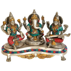 Brass Ganesh-Lakshmi-Saraswati idol trio on pedestal with teal and red accents