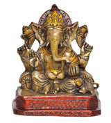 Lord Ganesha brass statue front view, golden face with crown, red patterned pedestal