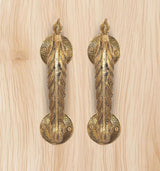 Close-up of golden brass peacock door handles on a light wood panel