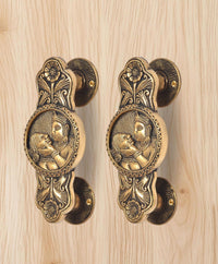 Brass door handle pair showing round rosettes and two-god & goddess oval relief design