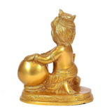 Brass Bal Krishna figurine holding laddu pot, seated on ornate pedestal, gold.