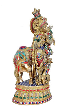 Brass Krishna on cow, side view with raised arm, ornate garlands, and patterned base