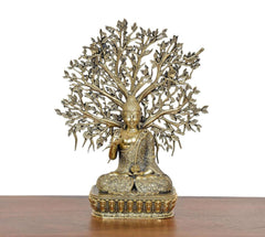 Brass-gold seated Buddha on ornate pedestal, surrounded by tall leaf-tree canopy