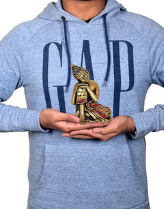 Brass Gautam Buddha idol held in hands on a person wearing a light gray hoodie
