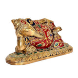 Close-up of lying brass Ganesha statue head and torso, red enamel with blue and green