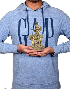 Brass Krishna statue on cow, held by person for size, flute and crown visible
