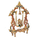 Brass Ganesh idol on swing seat with ornate red-green panels and central hanging bell