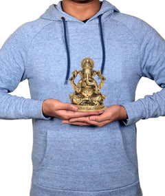 Gold-tone brass Ganesha idol held in hands, seated four-armed figure, ornate base