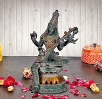 Saraswati brass sculpture holding veena, seated goddess with four arms, dark green patina