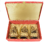 Open Diwali puja box with three brass deities on lotus flower stands: Lakshmi, Ganesh, Saraswati