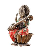 Brass Saraswati idol seated, holding veena and raising a hand; red jeweled lotus base