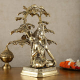 Brass Lord Shiva statue under tree, side view with detailed ornaments and raised trident