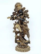 Brass Krishna idol holding a flute, dark figure with gold filigree, standing